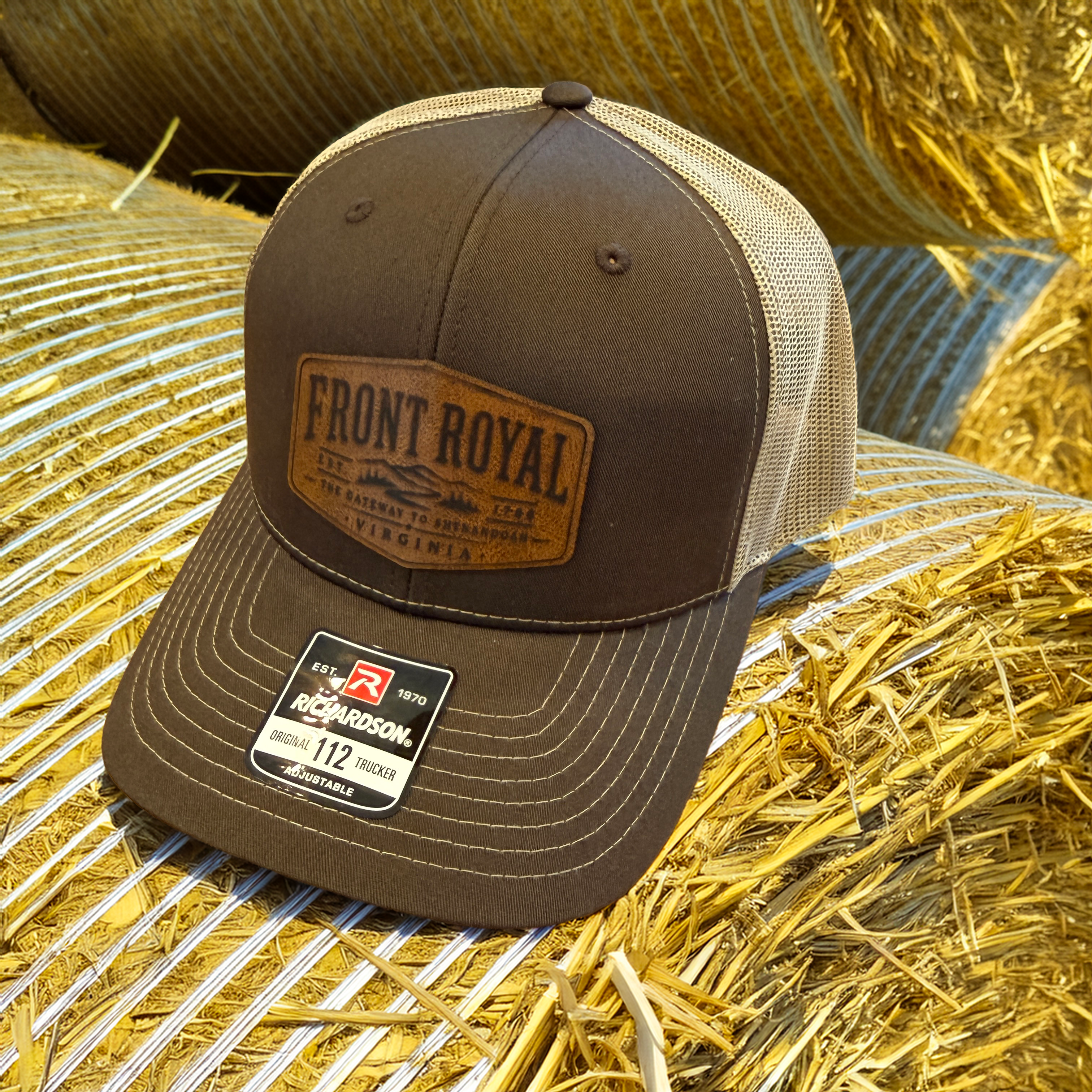Front Royal Virginia leather patch Richardson 112 trucker hat resting on hay bales in warm golden farm lighting.