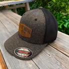 Front Royal Virginia leather patch Flexfit trucker hat photographed on a rustic wooden table with a natural outdoor backdrop.