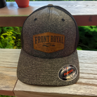 Front Royal Virginia leather patch Flexfit trucker hat displayed on a rustic wooden deck overlooking lush green trees.