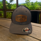 Front Royal Virginia charcoal Flexfit trucker hat with engraved leather patch photographed on a rustic deck overlooking the Shenandoah Valley.
