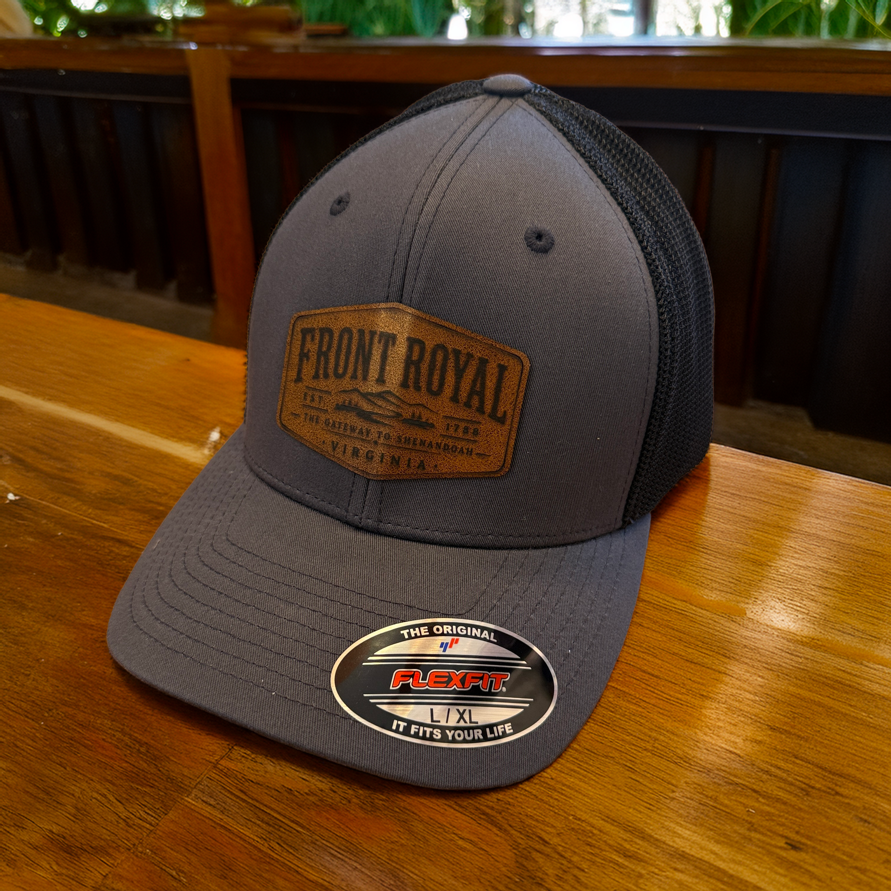 Front Royal Virginia charcoal Flexfit trucker hat with genuine leather patch resting on a polished wooden table.