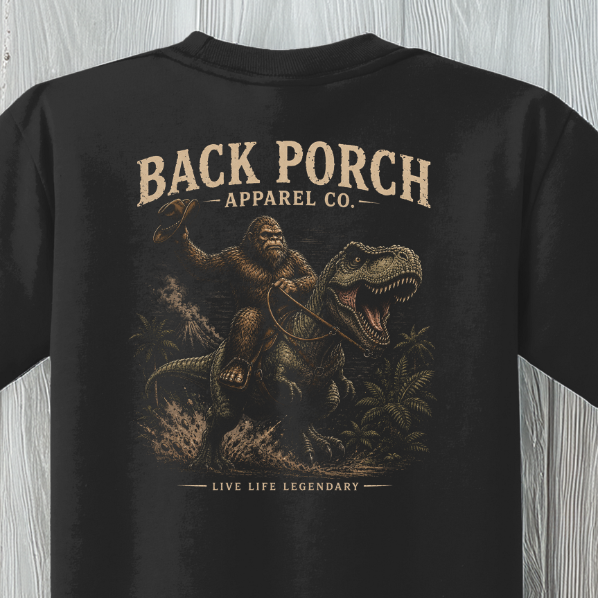 Close-up of the Youth Bigfoot Riding T-Rex graphic featuring Bigfoot riding a Tyrannosaurus rex with vintage artwork.