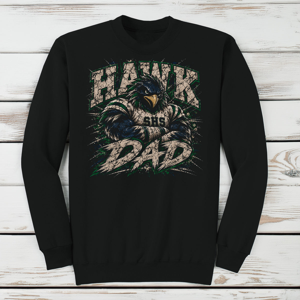 A black crewneck sweatshirt featuring a distressed graphic of a hawk mascot with the text 'HAWK DAD' and 'SHS' on the front, displayed flat against a white wood plank background.
