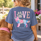 Woman wearing a denim-blue Simply Southern Dog Love T-shirt with a colorful patchwork golden retriever graphic, floral paw print, and LOVE lettering while sitting beside a dog.