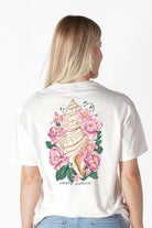 Woman wearing Simply Southern Floral Conch Shell short sleeve T-shirt showing detailed conch shell surrounded by pink flowers on the back