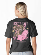 Model wearing Simply Southern black “Scrub Life” t-shirt with pink camo scrub graphic on back