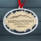 Shenandoah National Park layered wooden ornament with white snowflake frame, engraved natural wood badge, and red hanging ribbon displayed on a dark blue wood background.