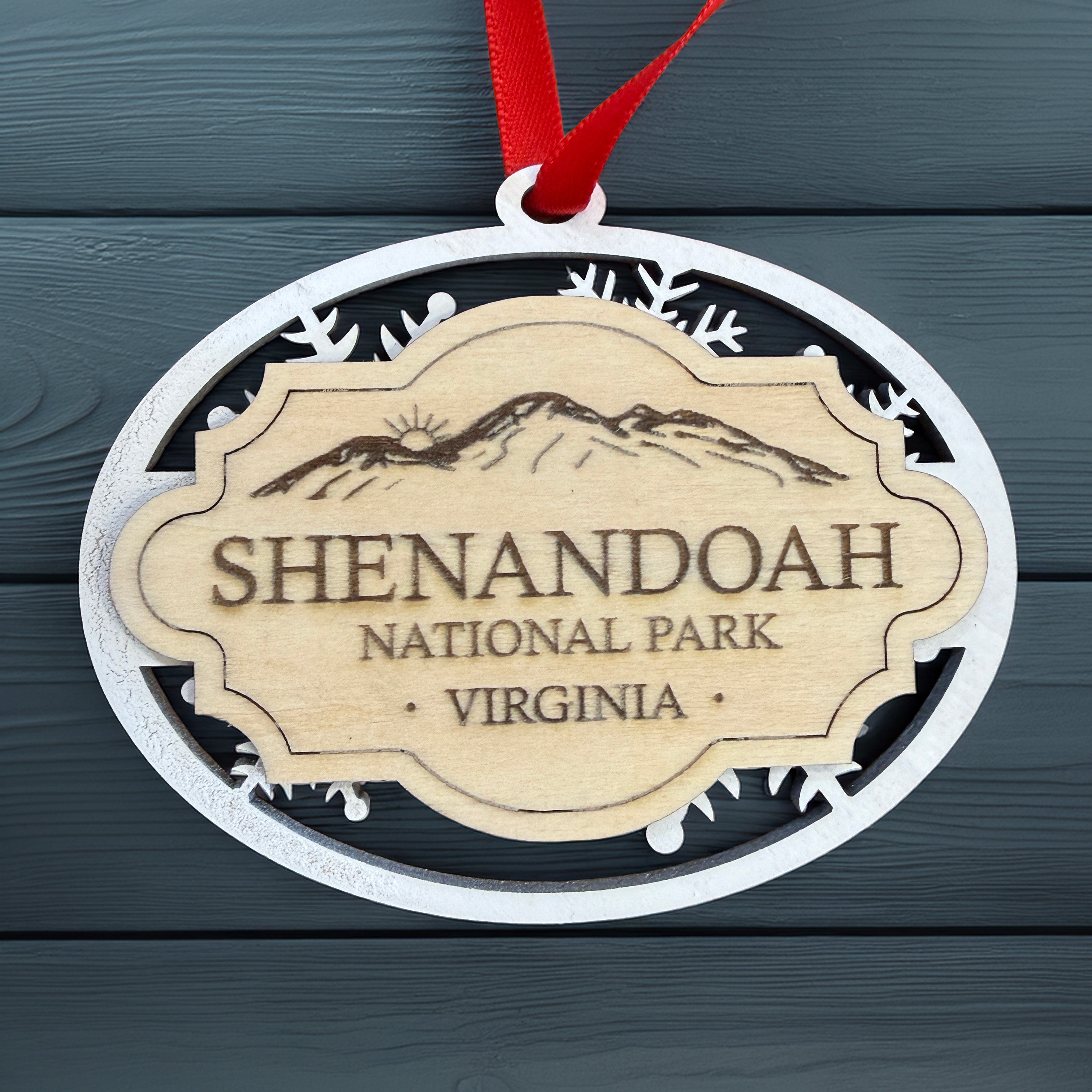 Shenandoah National Park layered wooden ornament with white snowflake frame, engraved natural wood badge, and red hanging ribbon displayed on a dark blue wood background.