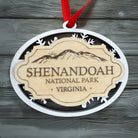 Handcrafted Shenandoah National Park Christmas ornament featuring a white snowflake design, engraved mountain artwork, and natural wood center plaque on a weathered gray wood background.