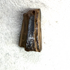 A raw, rough rectangular piece of dark brown wood or bamboo showing natural grain and a glossy black center, placed on a textured white surface.