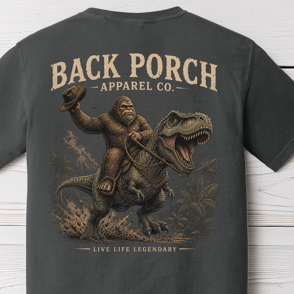 Bigfoot riding T-Rex graphic t-shirt on Comfort Colors garment-dyed tee featuring Sasquatch riding a dinosaur