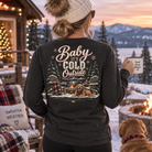 Woman wearing Baby It’s Cold Outside Comfort Colors Pepper long sleeve shirt at a snowy mountain cabin with golden retriever and fire pit