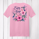 Enjoy The Little Things graphic t-shirt featuring colorful hummingbirds, pink flowers, and floral artwork on a soft pink shirt