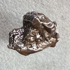 A small, rough, metallic lump of silver-colored metal, resembling raw sterling silver or pewter, photographed on a textured light gray background.