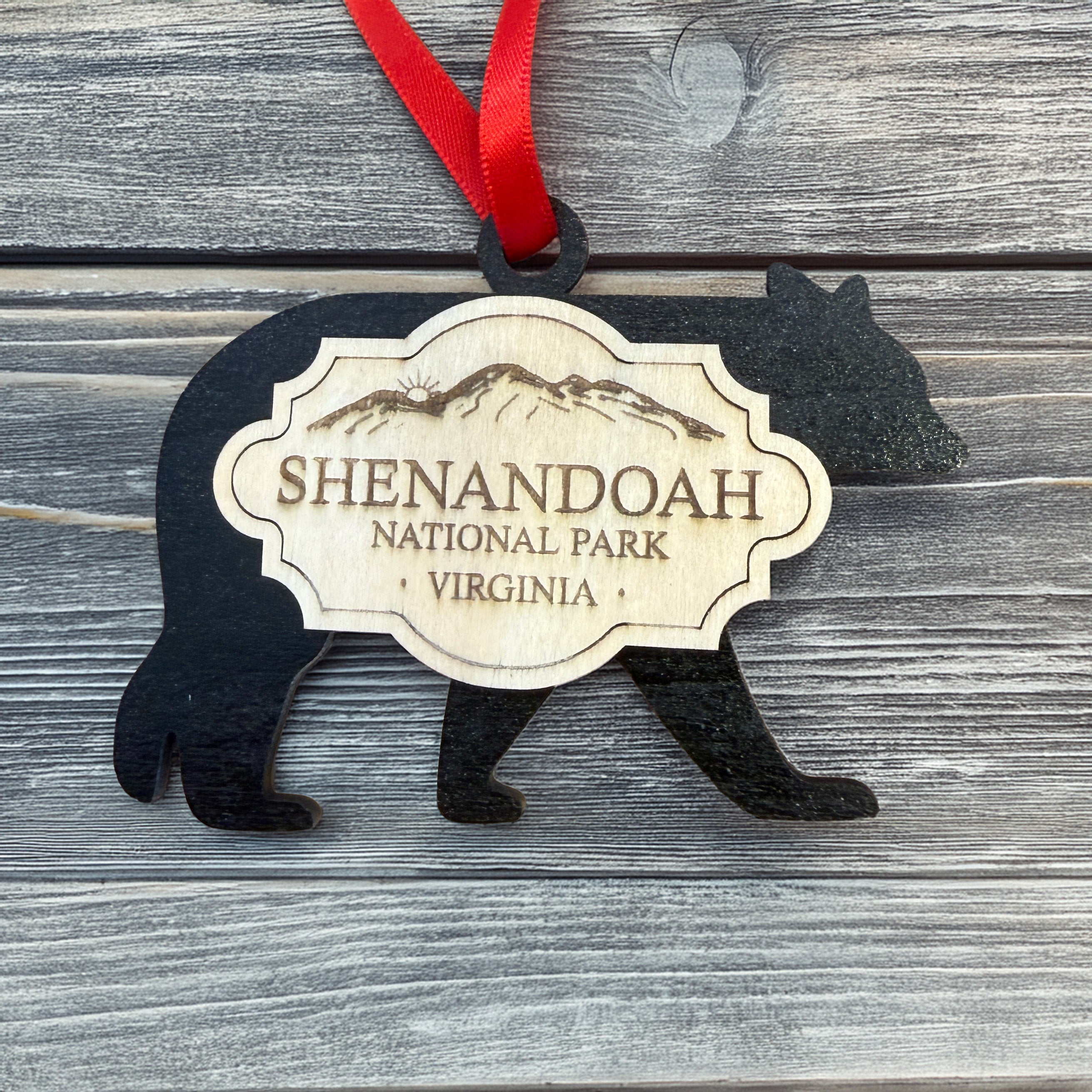 Handmade Shenandoah National Park bear ornament featuring a black bear silhouette, engraved wood badge, and red ribbon on a rustic gray wood background.